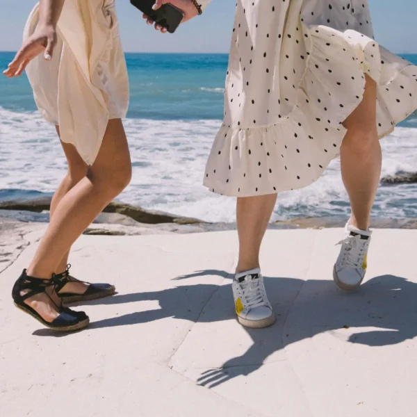 two young women in sundresses dance on the beach